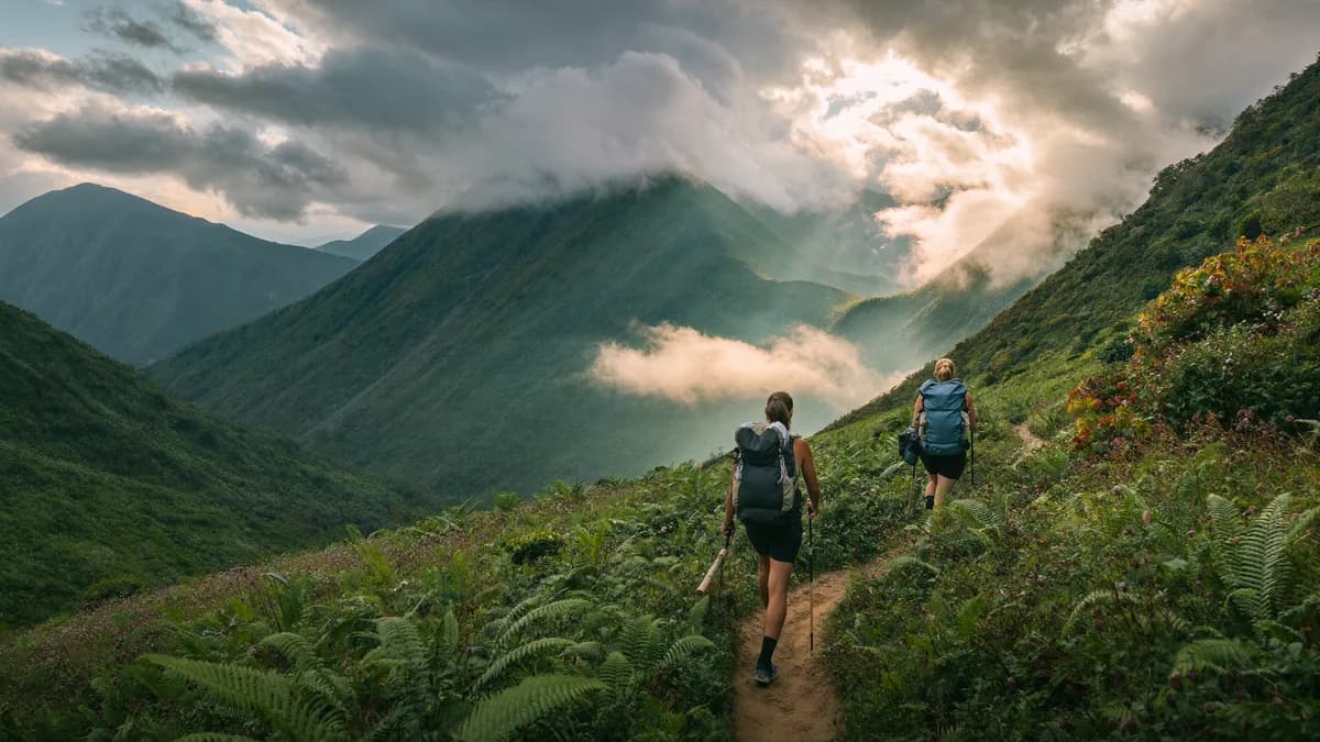 Dos senderistas con bastones de trekking avanzando por un sendero de montaña entre bosque de niebla y cordilleras andinas en Antioquia