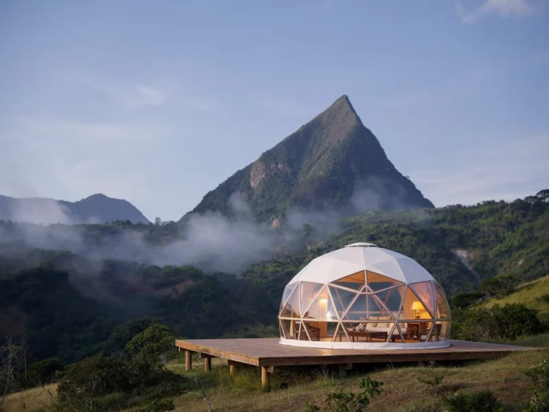 Domo de glamping de lujo frente al Cerro Tusa en Colombia, con ventanas transparentes, terraza de madera y niebla matinal