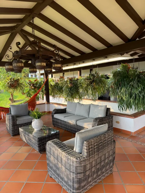 Sala social exterior de La Juana con muebles de mimbre, hamaca y helechos colgantes